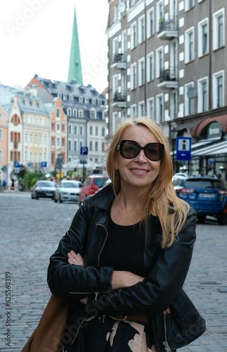 Smiling woman. A woman in the city. A woman in a black leather jacket. A woman in sunglasses. Modern woman. Beautiful woman. Model plus fifty.