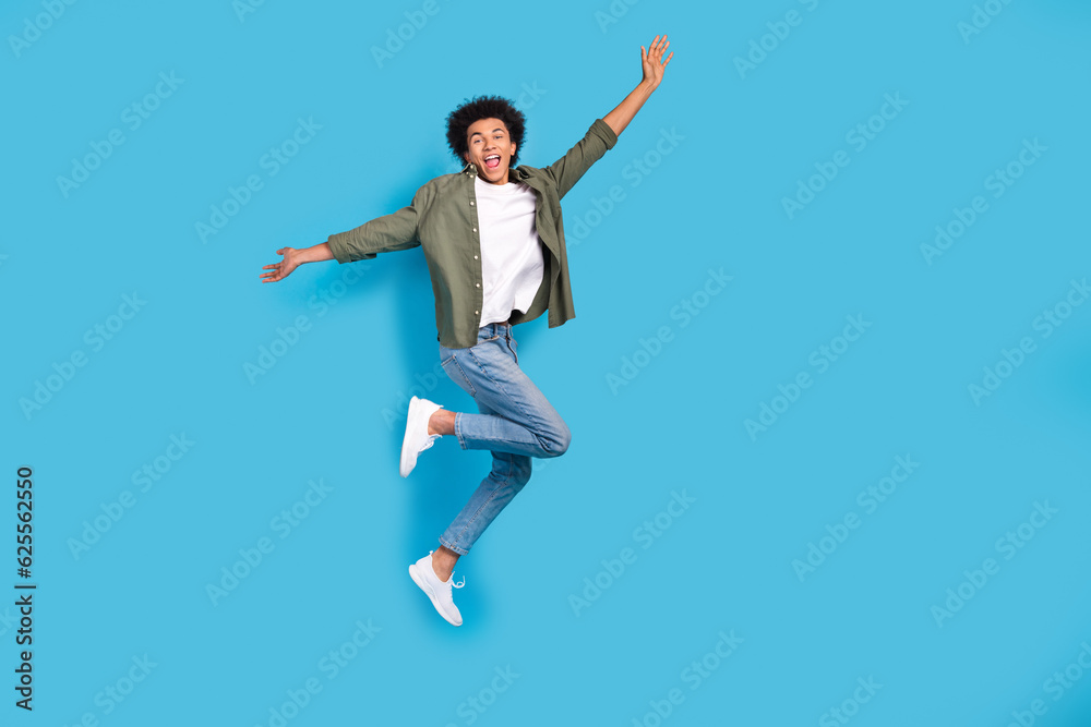 Full length portrait of overjoyed cheerful man jumping empty space isolated on blue color background