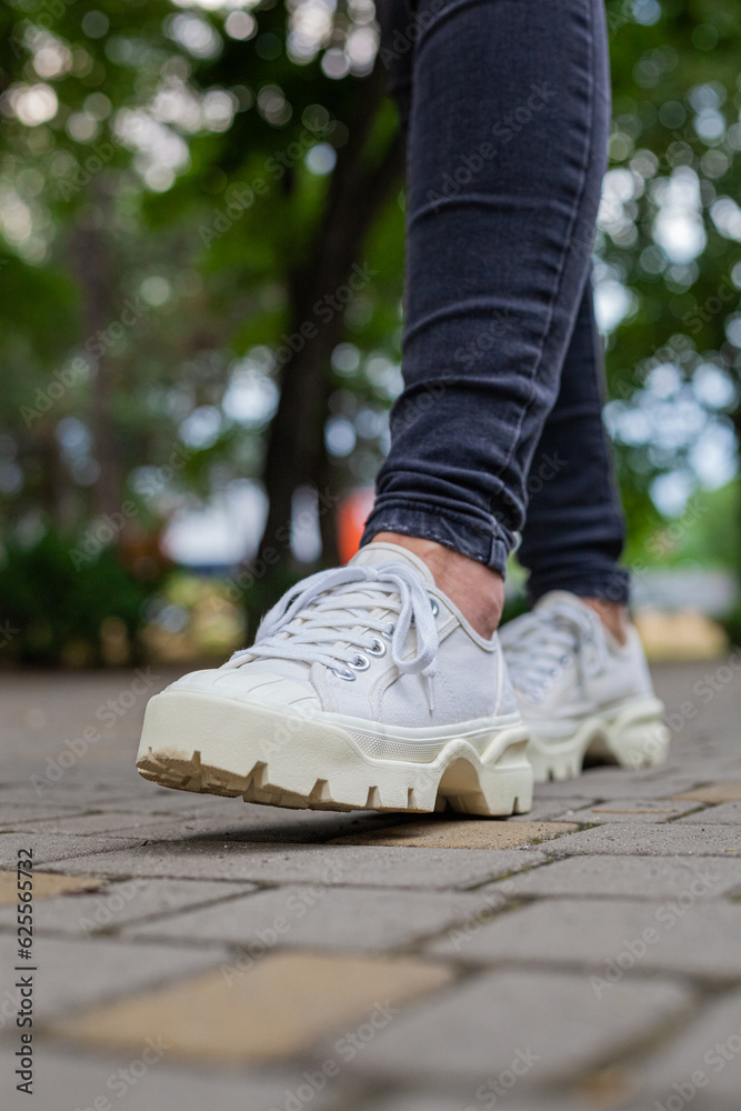 White sneakers with studded soles on female legs in black jeans