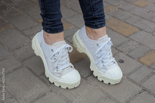 White sneakers with studded soles on female legs in black jeans