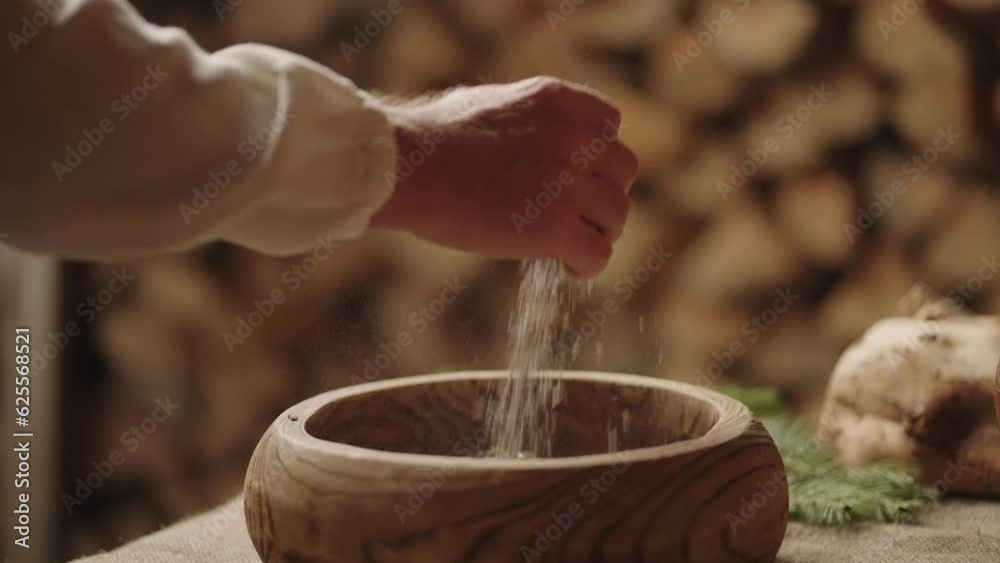 Man Taking Grain From Wooden Bowl On Table In House Of Old Slavic Village, Old Ukrainian Style Man Taking Grain From Wooden Bowl On Table In House Of Old Slavic Village, Old Ukrainian Style