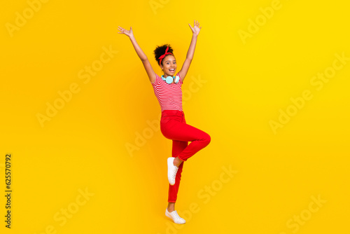 Full body photo of pretty young girl celebrate raise hands music dressed stylish red striped outfit isolated on yellow color background