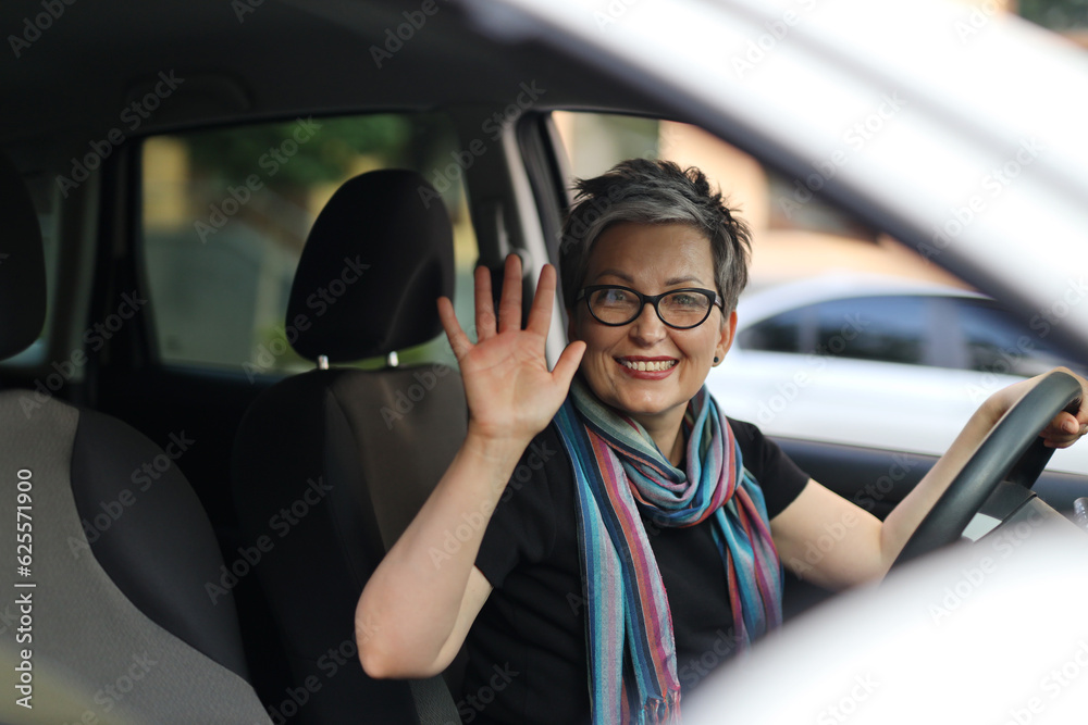 Cheerful mature positive woman driving a car waving her hand. Cheerful mature positive woman driving a car waving her hand.