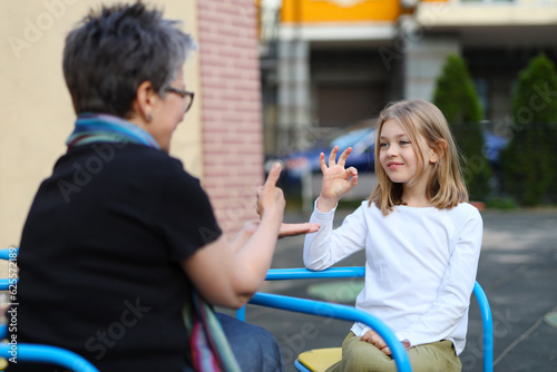 A deaf child communicates in sign language with a teacher on the playground.