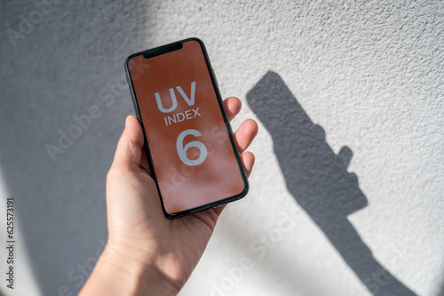 Smartphone in person hands with application showing UV index outside at sunny day