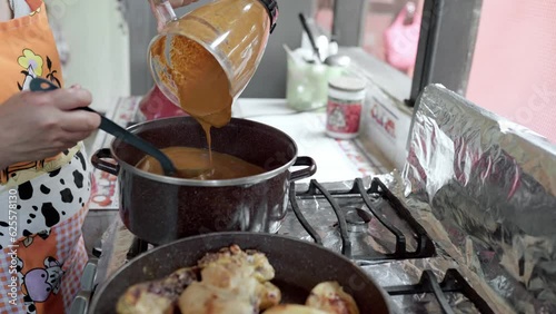 An adult Hispanic woman is pouring mole sauce from a blender into a pot