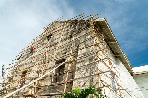 A Filipino workman on bamboo scaffolding,redecorates the end wall of Oslob Church,high above the ground,Cebu,Philippines.