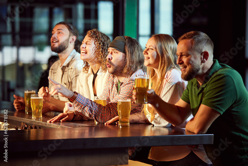 Cheerful people, friends sitting in bar, attentively watching football match translation, drink,ing beer, having fun. Concept of sport competition, hobby, lifestyle, human emotions, fun