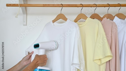 An unrecognizable woman steams a t-shirt hanging on a wooden hanger