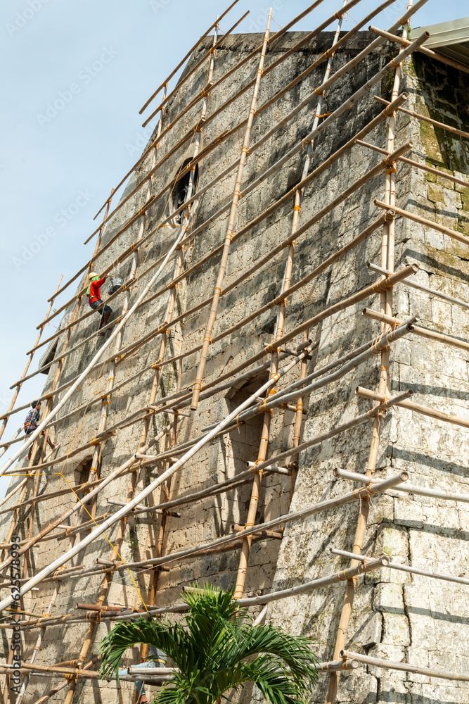 A Filipino workman on bamboo scaffolding,redecorates the end wall of Oslob Church,high above the ground,Cebu,Philippines.