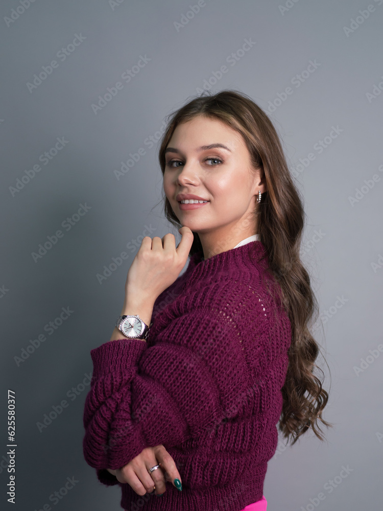 Obraz premium Portrait of a beautiful young woman in a purple sweater on a gray background