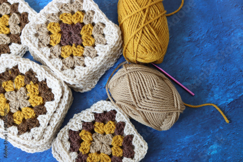 Crocheted granny squares made of natural brown  mustard and beige wool. Soft and fluffy crochet ornament on blue textured background. 