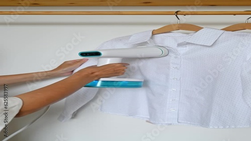 An unrecognizable woman steams a t-shirt hanging on a wooden hanger