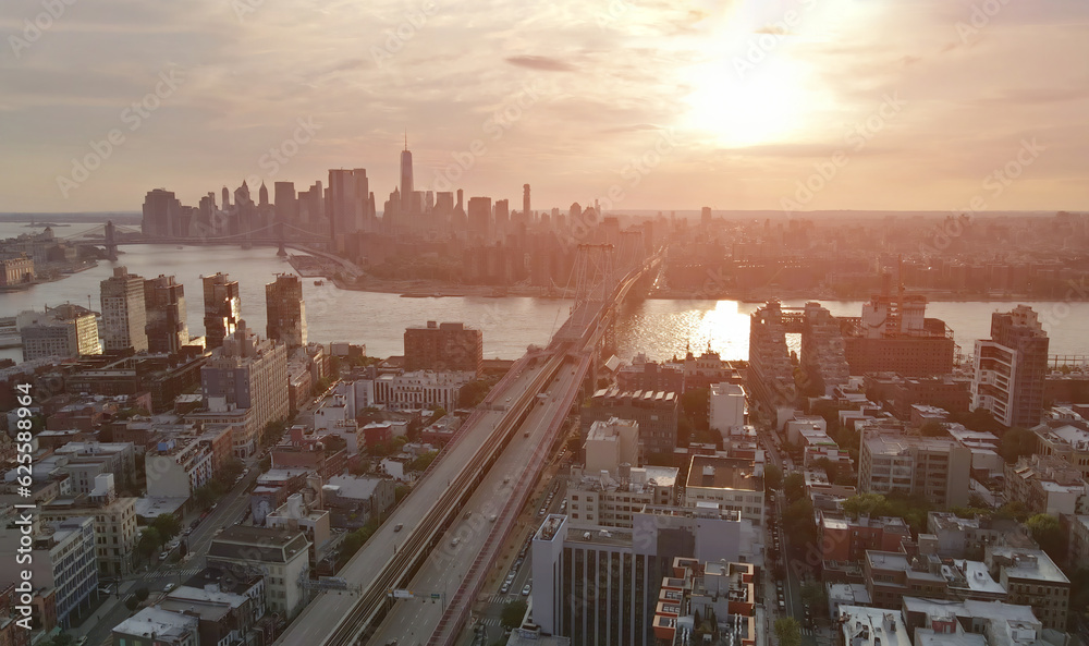 During sunset, New York City Manhattan skyline, visible across East River, is magnificently framed by Williamsburg Bridge.