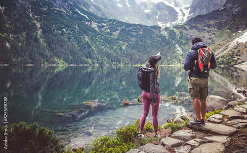 A couple of tourists during a trip to the mountains by a mountain lake. Girl pointing towards the mountain.