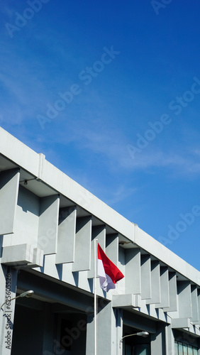 Indonesia flag fluttering on a pole in front of the gray building. Indonesian state flag, red and white. Blue and clear sky. © Aldaufaira