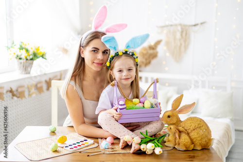 easter, a mother with a little daughter with hare ears on her head are preparing for the holiday by gently hugging and kissing and spending time together, colorful eggs, lifestyle,