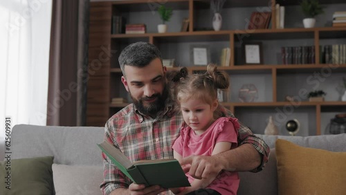 Young father and daughter read intersting book at home. Loving parent bearded man teaches his preschool child to read. Daddy reading fairy tale story. Parenthood, love and happy family concept. photo