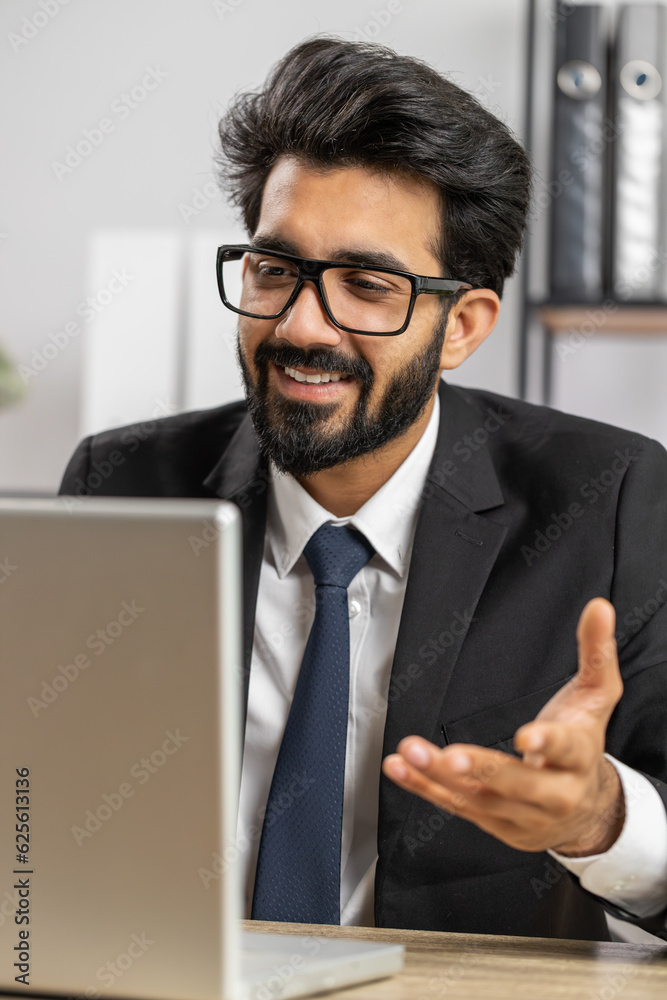 Indian businessman working on laptop computer at home office desk talk on online communication video call with employee, boss. Manager man freelancer support services looking at webcam of computer Indian businessman working on laptop computer at home office desk talk on online communication video call with employee, boss. Manager man freelancer support services looking at webcam of computer