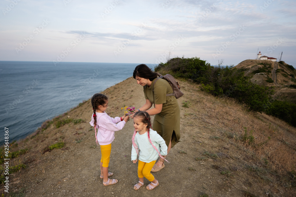 Mother and two daughters with wild flowers against sea from the top of the mountain. Cape Emine, Black sea coast, Bulgaria. Mother and two daughters with wild flowers against sea from the top of the mountain. Cape Emine, Black sea coast, Bulgaria.