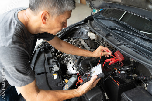 A middle age Asian male mechanic using a battery checker to check on the car battery status