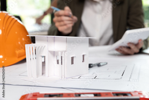 Scale model house on table with helmets and female architect working. House model on desk over confident of architect working in a office.