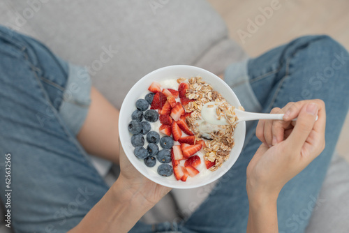 Asian Woman having delicious healthy breakfast at home on morning. Health care female eats yogurt with granola and berry fruit. Healthy food, Vitamins, clean diet, dieting, detox, organic food.