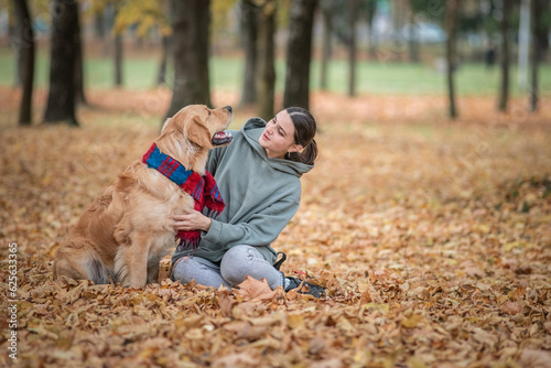 Portrait of a beautiful dark-haired girl with a golden retriever in the autumn park.