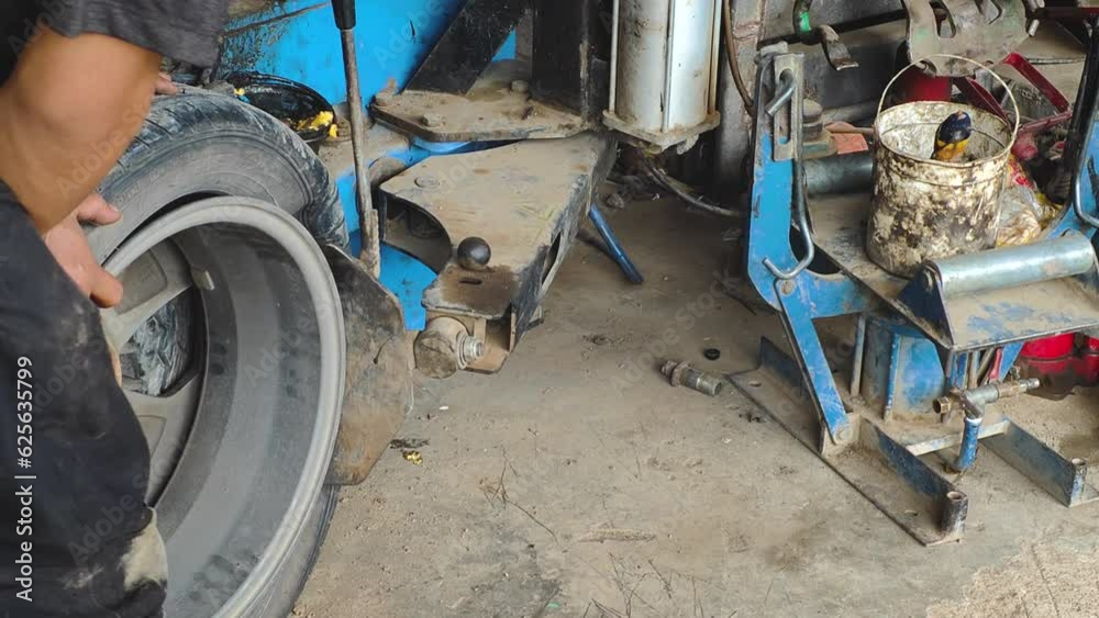 A car mechanic uses an automated machine to pull tires off wheels to change tires in a garage. concept of car repair service Replacement of damaged tires, repair and maintenance of cars. A car mechanic uses an automated machine to pull tires off wheels to change tires in a garage. concept of car repair service Replacement of damaged tires, repair and maintenance of cars.