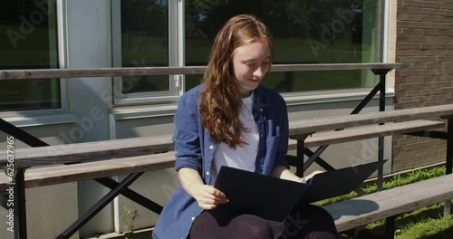 Happy student sitting on bleachers while studying in front of a school