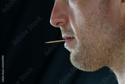Man with a toothpick in his mouth close up profile face, background selective focus, copy space people theme, story tel8ng. photo