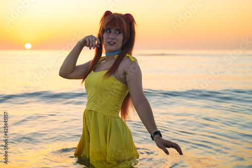 Italian girl cosplay Asuka Langley Soryu from the anime Neon Genesis Evangelion. Woman by the sea dressed in yellow. Blue eyes and red hair. photo