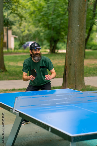 Inclusiveness An elderly focused man with long hair and a gray beard plays ping pong in a city park  © Guys Who Shoot