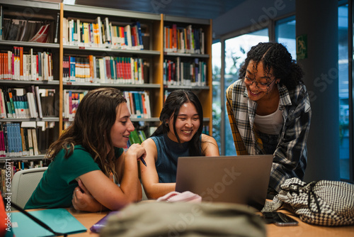 Three college students using a laptop at the university library. They are preparing for a exam.