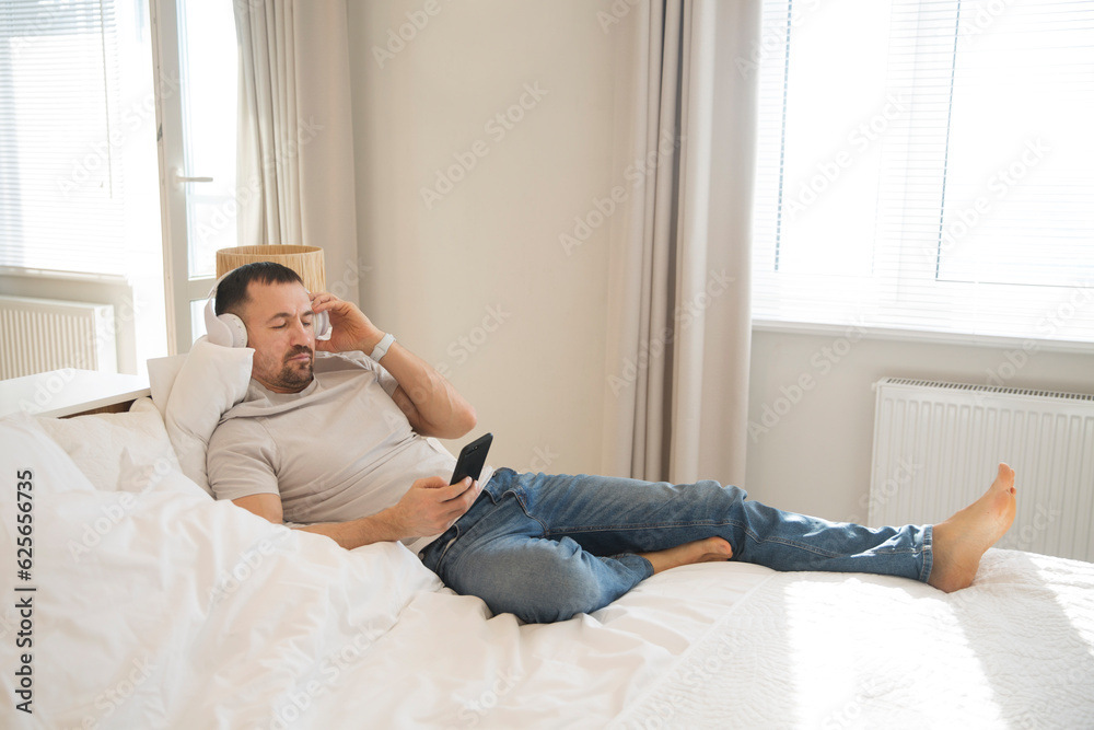 man wearing headphones  with mobile phone relaxed on the bed of your apartment. concept without stress. mental health. work from vacation home