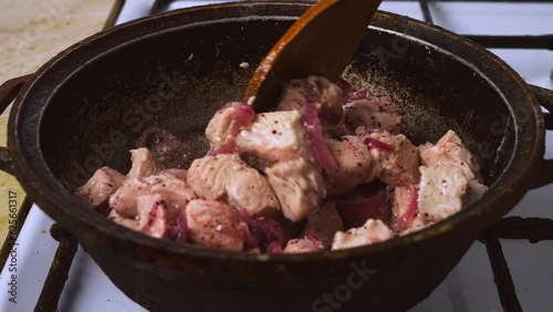 Chicken pieces with red onion and sumac in a pan are mixed with a wooden spatula. Medium plan photo