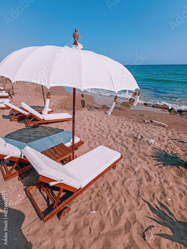 Wooden deck chairs with mattresses and beach umbrellas on sandy beach by the sea