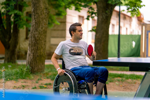 Inclusiveness A disabled man in a wheelchair plays ping pong in a city park against a backdrop of trees 