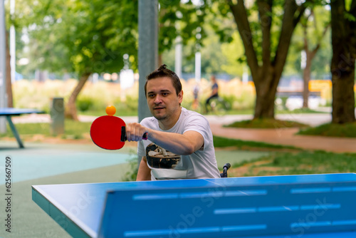 Inclusiveness A disabled man in a wheelchair plays ping pong in a city park against a backdrop of trees  © Guys Who Shoot
