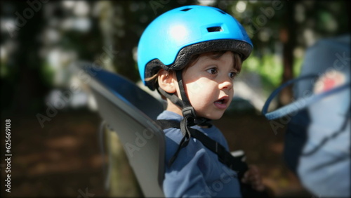 Child wearing helmet in bicycle back seat riding bike with parent