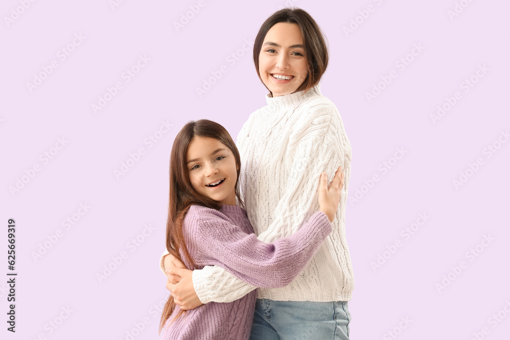 Little girl and her mother in warm sweaters hugging on lilac background Little girl and her mother in warm sweaters hugging on lilac background