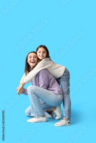 Little girl and her mother in knitted sweaters hugging on blue background