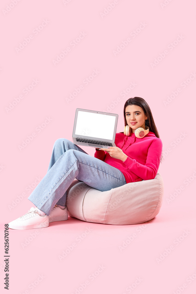 Young female programmer with laptop sitting on beanbag against pink background Young female programmer with laptop sitting on beanbag against pink background