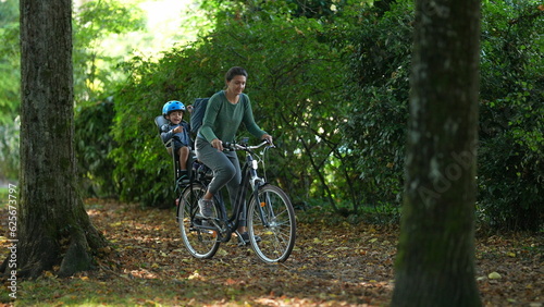 Mother riding bicycle with child in bike back seat outside in nature