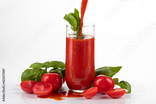 tomato juice in a glass goblet with tomatoes lying nearby on a white background