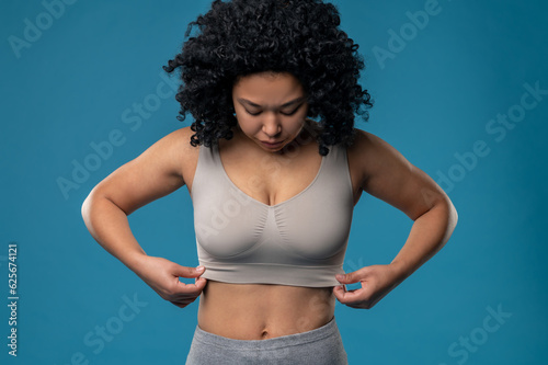 Waist up picture of woman in a bra standing on a blue background