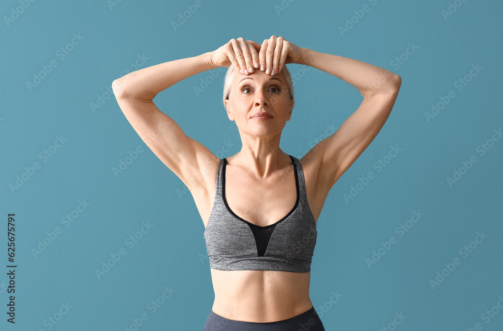 Sporty mature woman doing face building exercise on blue background Sporty mature woman doing face building exercise on blue background