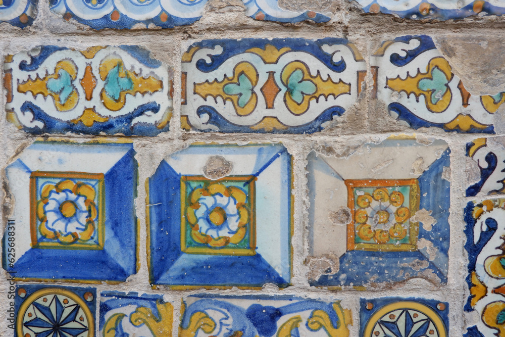 Old damaged tiles with floral ornate painted in Spain. Real textured multi coloured ceramic background. Vivid colours remains. Vintage architectural details