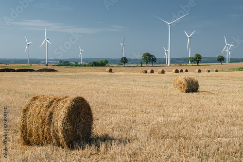 Green energy and agriculture: field with heaps of hay and wind turbines