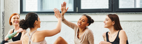 Free Download young, carefree and excited african american woman giving high five to friend near cheerful women during yoga class in gym, friendship, harmony and mental health concept, banner - GFXLoad